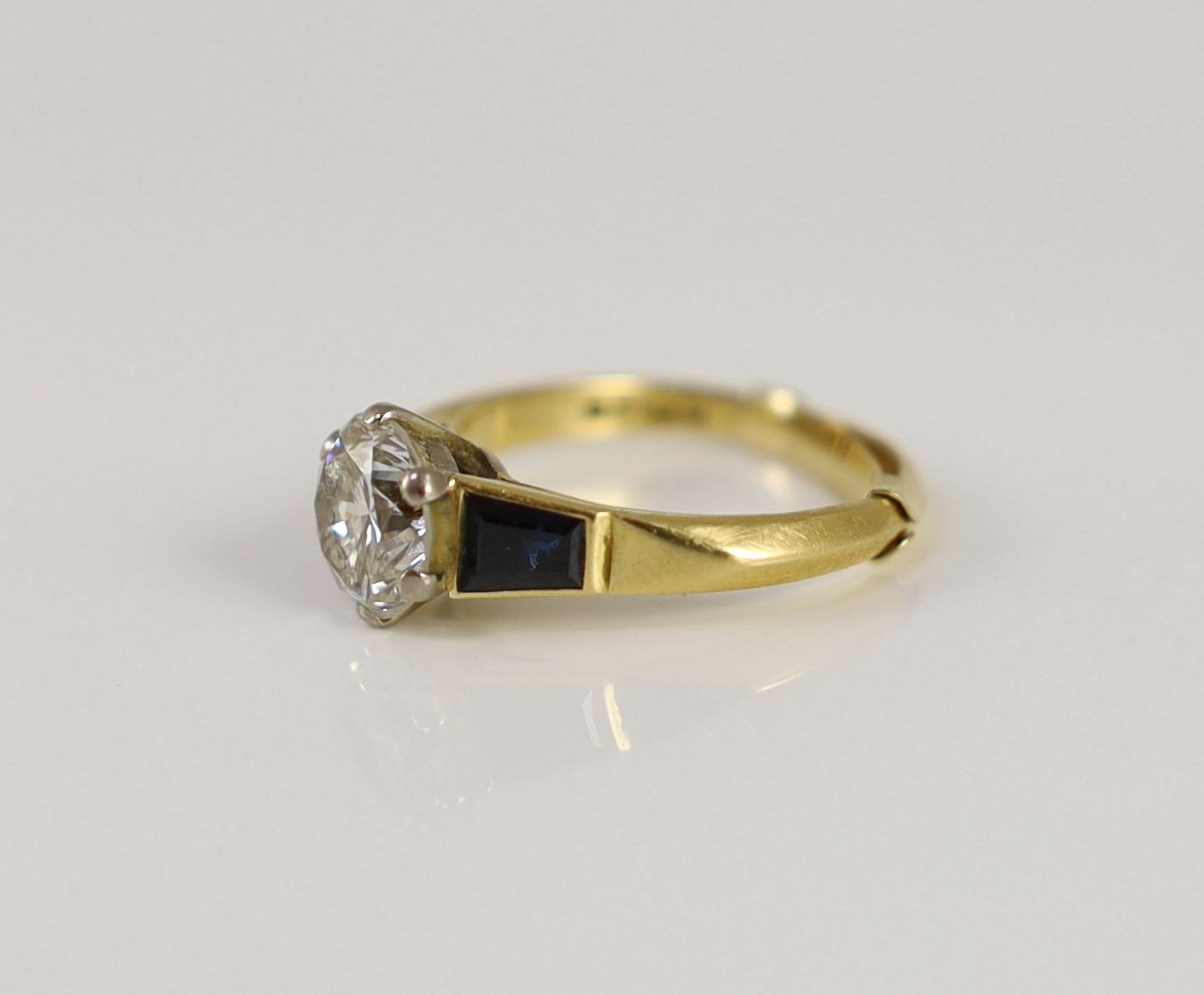 A modern 18ct gold and single stone diamond ring, with trapeze cut sapphire set shoulders